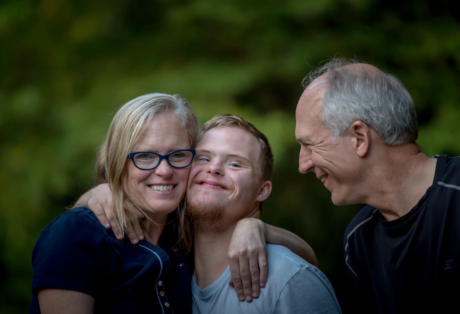 Parents with their adult son, smiling together outdoors